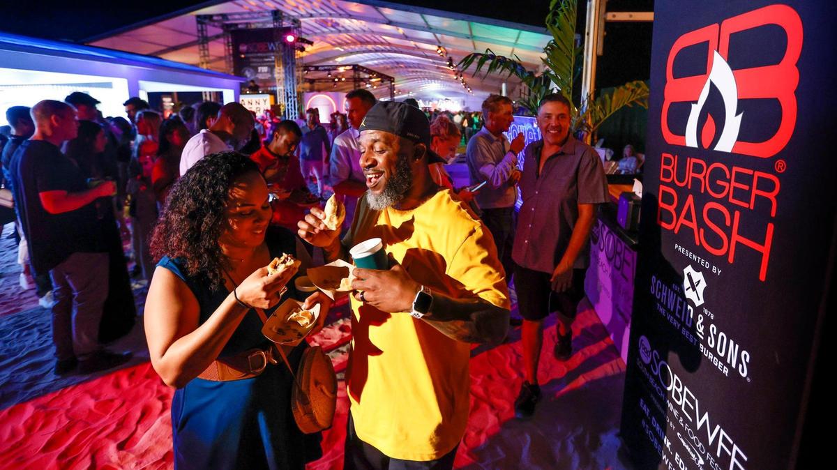 Dana and Efren Johnson try out a couple of burgers during the 2023 Burger Bash at the South Beach Wine & Food Festival on the sand by the Ritz-Carlton Miami Beach.