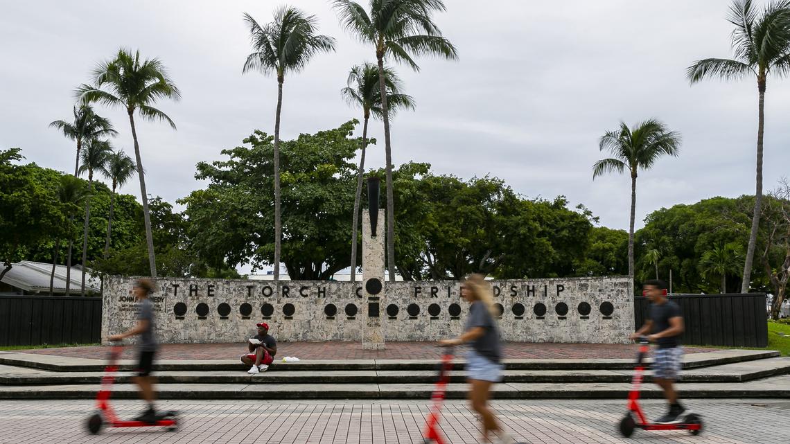 Scooter riders pass the non-functional Torch of Friendship in downtown Miami on Nov. 7, 2019.