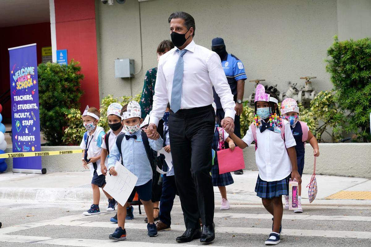 Miami-Dade Schools Superintendent Alberto Carvalho, center, walks with students Oliver Angel, left, and Ariah Olawale, right, outside of iPrep Academy on the first day of school, Monday, Aug. 23, 2021, in Miami. Schools in Miami-Dade County opened Monday with a strict mask mandate to guard against coronavirus infections.