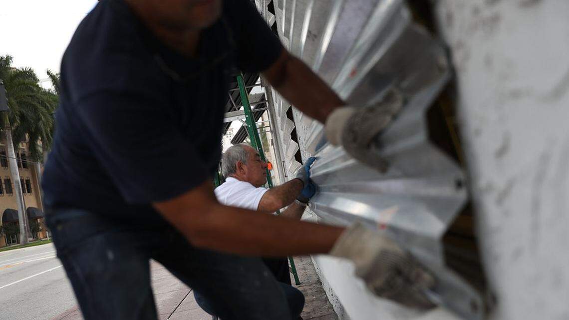 Men put window shutters in place as a storm bears down.