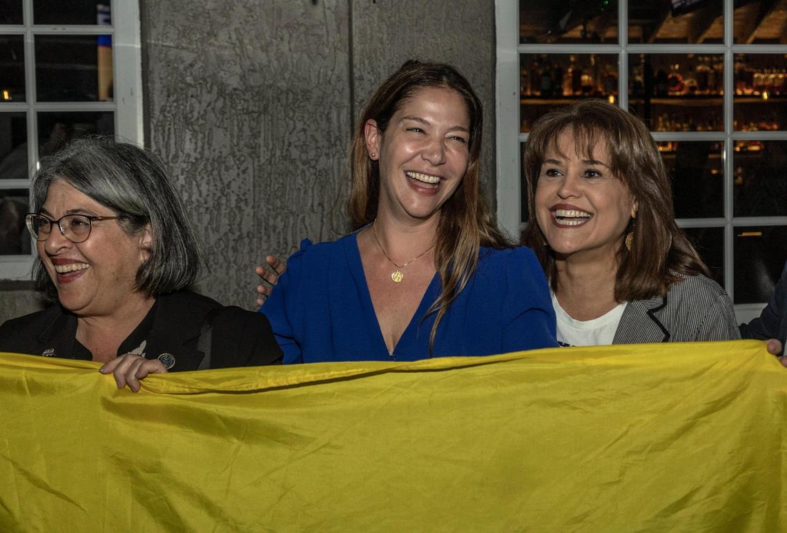 Miami, FL- February 27, 2023 -Sabina Covo,center, the winner of the District 2 special election in the city of Miami poses with a Colombian flag as she celebrates along with Miami Dade County Mayor Daniella Levine Cava , left and Annette Taddeo, right, during a party at The Taurus in Coconut Grove, 3540 Main Highway, Miami, FL 33133