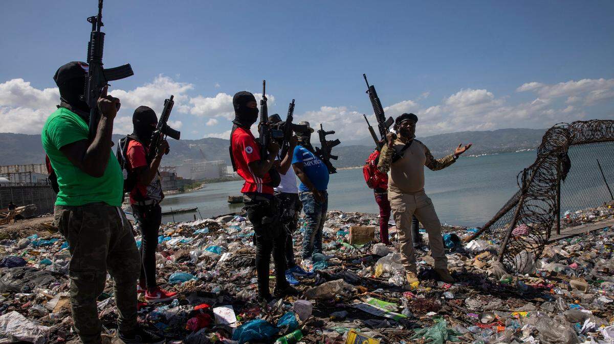 Flanked by members of the G9 gang coalition, leader Jimmy Cherizier, aka Barbecue, right, talks to reporters near the perimeter wall that encloses Terminal Varreux, the fuel port in Port-au-Prince, Haiti, Oct. 6, 2021.