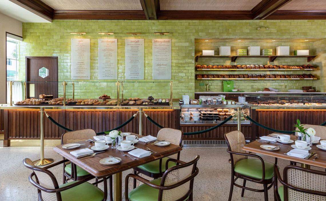 Glass cases are full of baked goods in front of a bright green wall at The Hive Bakery & Cafe in Palm Beach, Florida. Cafe tables fill out the dining area in front of the pastry cases.