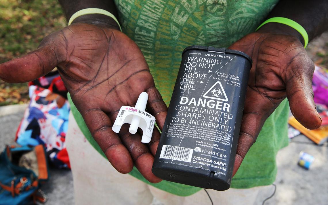 Philip Sylverin, who lives on the streets of Overtown, holds a Narcan nasal spray dispenser and a box where needles can be safely deposited. Both items were given to him by the IDEA Needle Exchange.