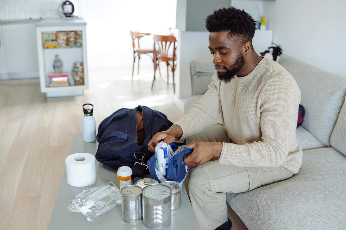 A man organizes emergency essentials, including canned foods, toiletries and supplies into a bag. It’s wise to gather your supplies into a hurricane kit before a storm approaches your area.