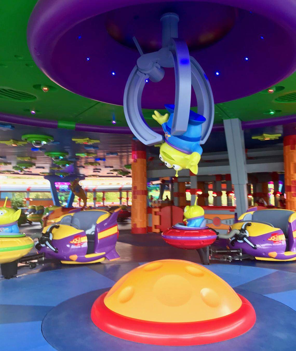 The. claw has grabbed onto a little green alien and holds it over the Alien Swirling Saucers ride in Toy Story Land.