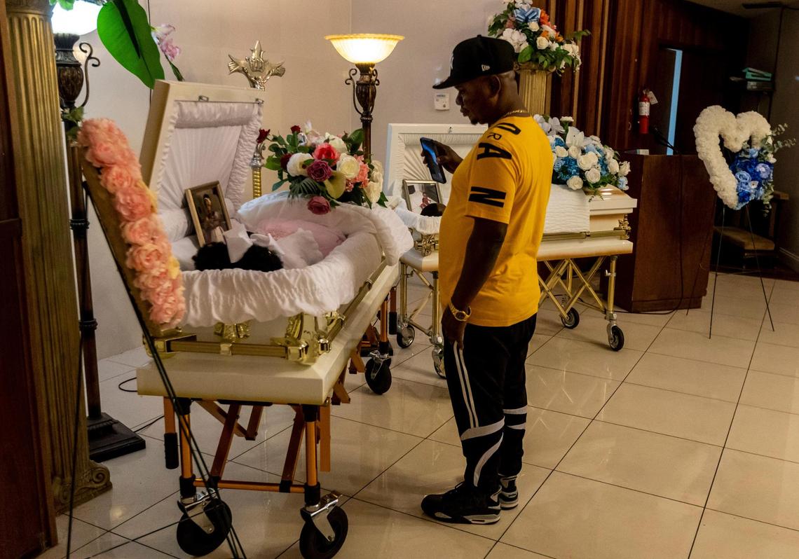 Frantzy Belval, father of Laura and Jeffry Belval, holds a cell phone in front of one of the caskets so a relative can see the children during the viewing.
