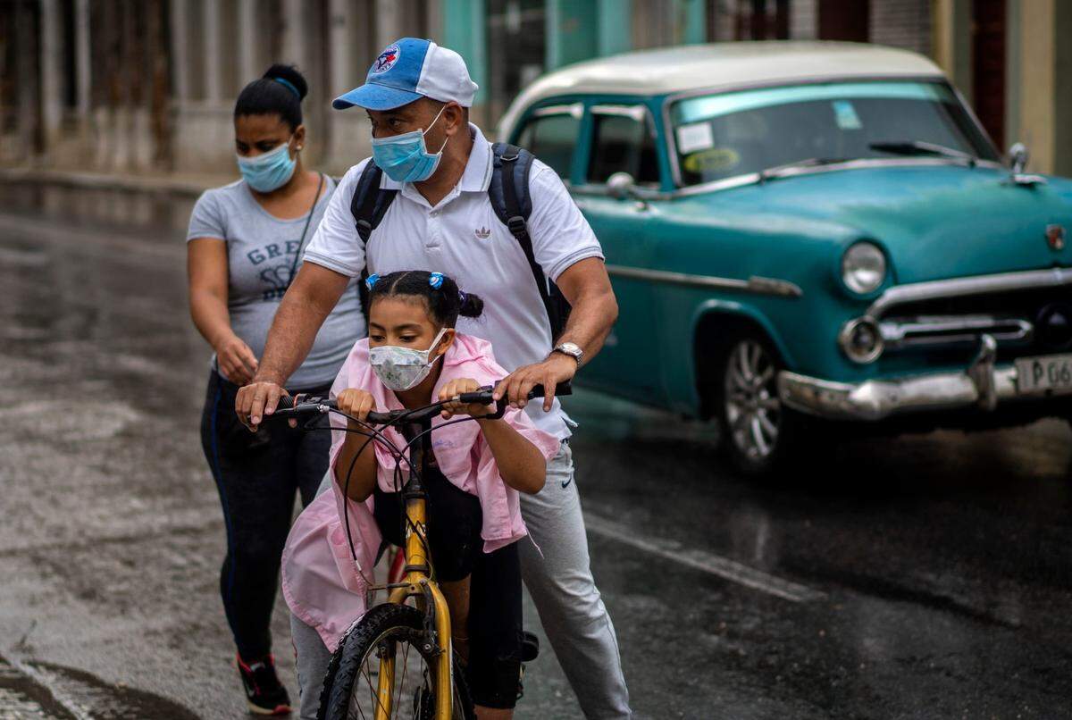 A girl wearing a mask against the spread of the new coronavirus is carried on the bicycle by her father in Havana, Cuba, Tuesday, Oct. 6, 2020.