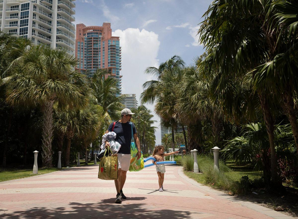 Weston Zamora, left, and Zoey, from Miami, walk to South Pointe beach in 90-plus temeratures on Thursday, July 13, 2023 in South Beach. “We’re trying to find cover in the shade,” Weston said.