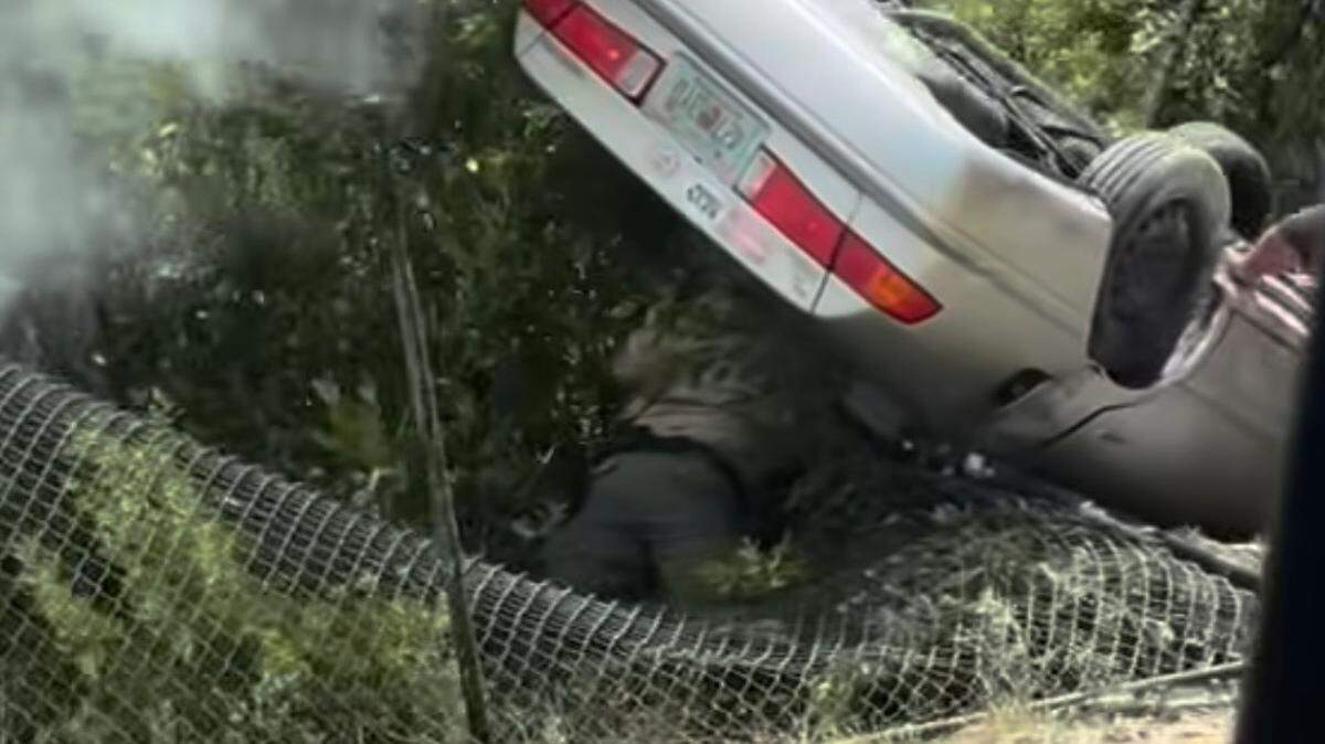 A Florida Fish and Wildlife Conservation Commission police officer crawls through the back windo of an overturned sedan that crashed through a fence on the side of the 18 Mile Stretch of U.S. 1 in Key Largo Wednesday, Aug. 20, 2025.