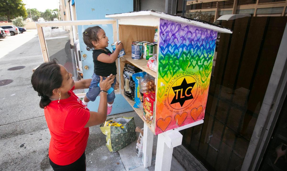 On Oct. 7, 2021, the Legacy Closet cut the ribbon on a little pantry that was installed in front of the Cutler Bay location by B’Nai Torah Congregation’s TLC Little Free Pantry. The concept is take what you need, leave what you can. Pictured, Layra Abuyot lifts her 19-month-old daughter, Mayla Santana, up so that she can help stock the pantry with donated food items.