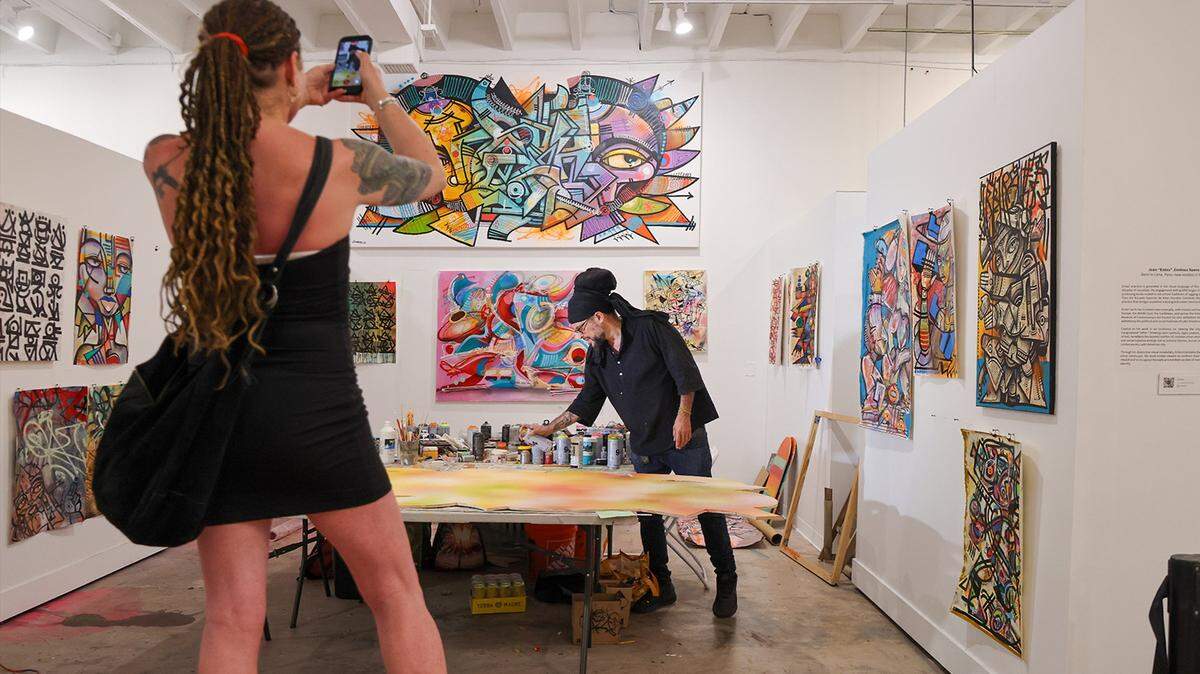 Artist Laura Page, who is visiting from Brooklyn, NY, left, stands on a bench to record James “Ras Terms” Monk as he works on a piece at The Museum of Graffiti Artist Studios in Wynwood, Miami, Tuesday, April 7, 2026. 