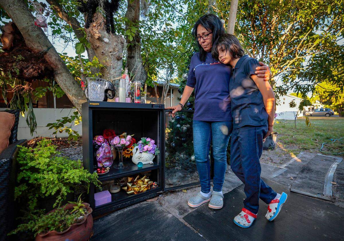 Georgina Sao brought her granddaughter, Gillian Rodriguez, back from Cuba to Miami after Gillian’s mother died from cancer. Grandmother and granddaughter stand next to a memorial for Gillian’s mother containing the urn with her ashes at their trailer home in Miami Gardens.