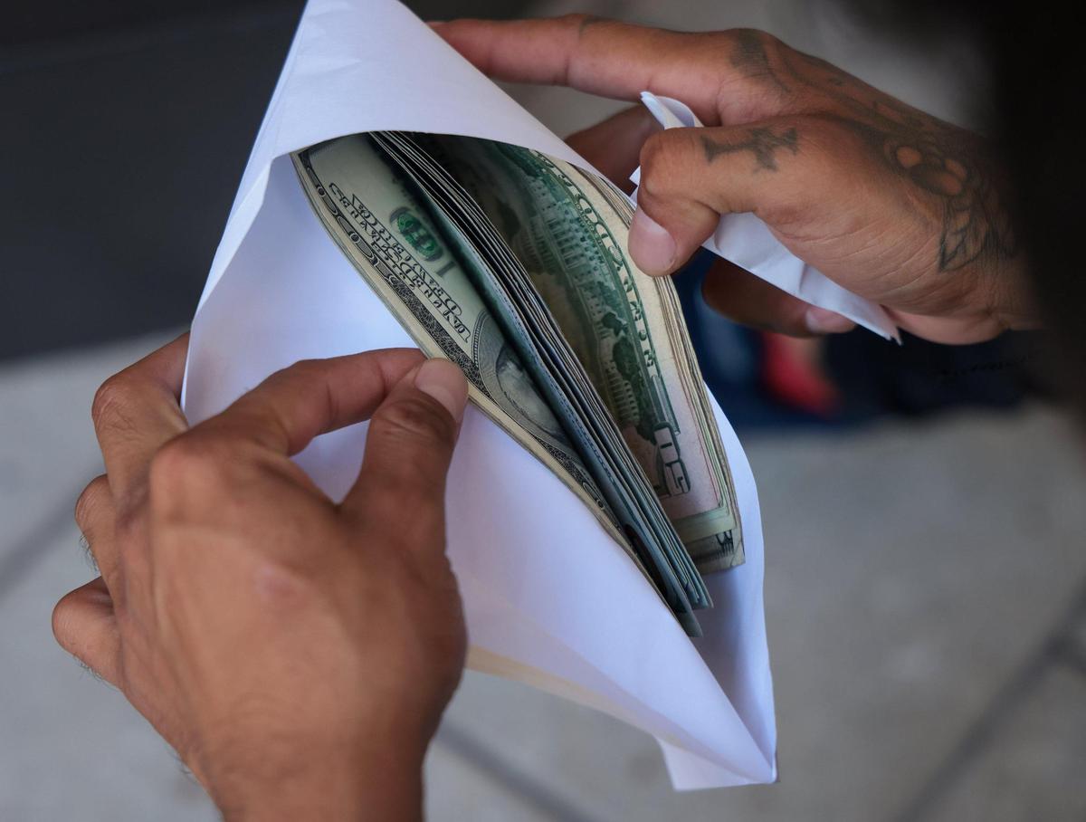 Pedro Escalona, de 24 años, a la derecha, cuenta su dinero después de que su antiguo empleador le cobrara el cheque el martes 11 de octubre de 2022.