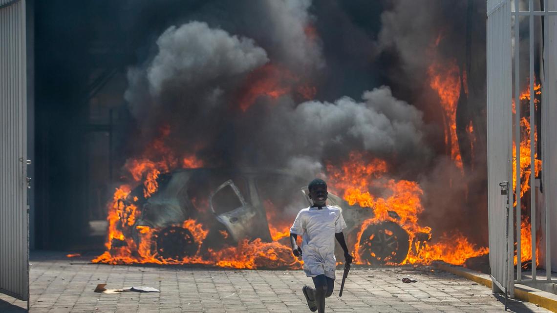 A boy runs out from the Nissan auto dealership set ablaze during a protest in Port-au-Prince, Haiti, Wednesday, March 17, 2021. The protests started when officers and police academy cadets marched toward police headquarters to demand that the bodies of several officers killed during a raid last week on the Village of God shantytown be recovered from the gang still holding them.