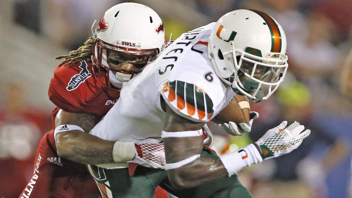 Miami Hurricanes wide receiver Herb Waters is tackled by Florida Atlantic defensive back Cre’von LeBlanc after an 11-yard gain in the first quarter at FAU Stadium in Boca Raton on Friday, Sept. 11, 2015.
