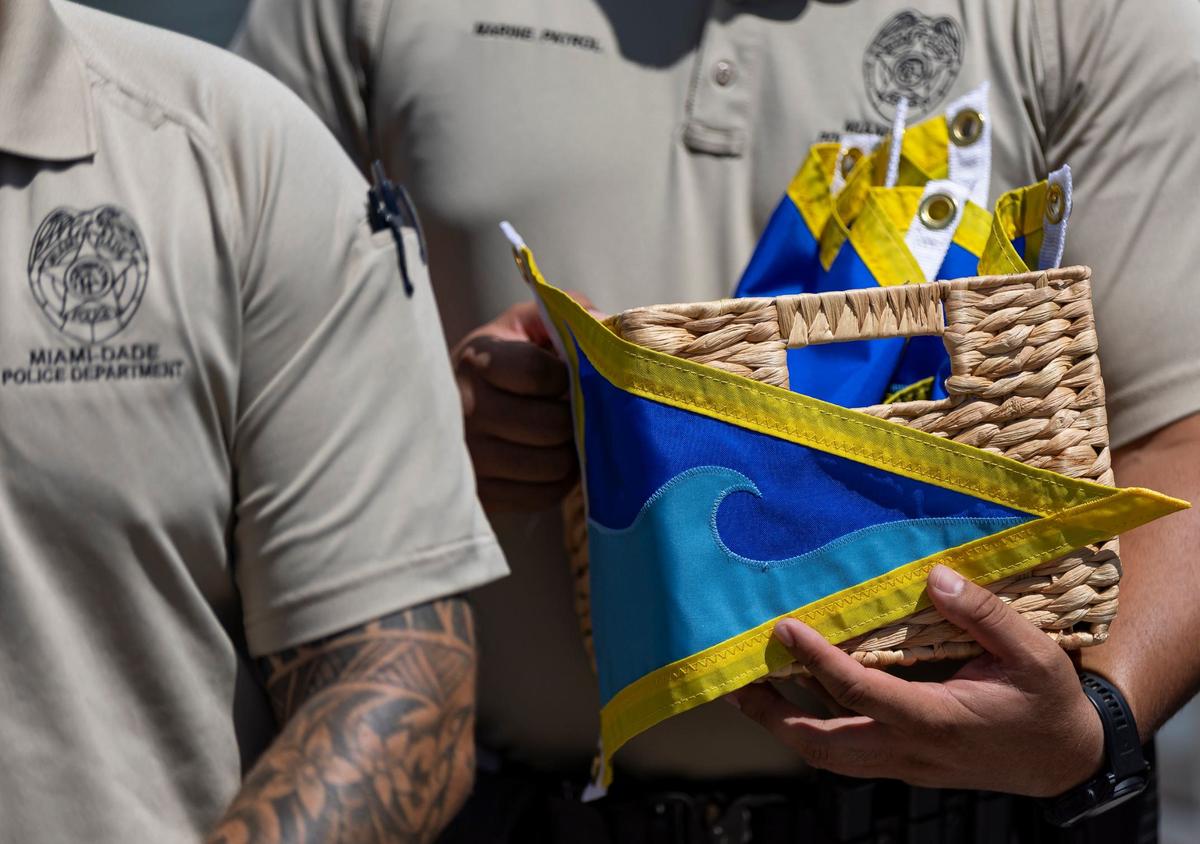 Miami-Dade Officer Ricaurte Lugo holds a box of Fly High, Bird flags as his team works to hang them on patrol boats at Black Point Park and Marina on Friday, Aug. 30, 2024, in Homestead, Fla. The flags were given to the officers by Melissa and Andres Fernandez, who started the Lucy Fernandez Foundation after their daughter was killed in a boat crash two years ago. They hope to raise awareness about boat safety with the flags that will hang on Miami-Dade Police vessels.