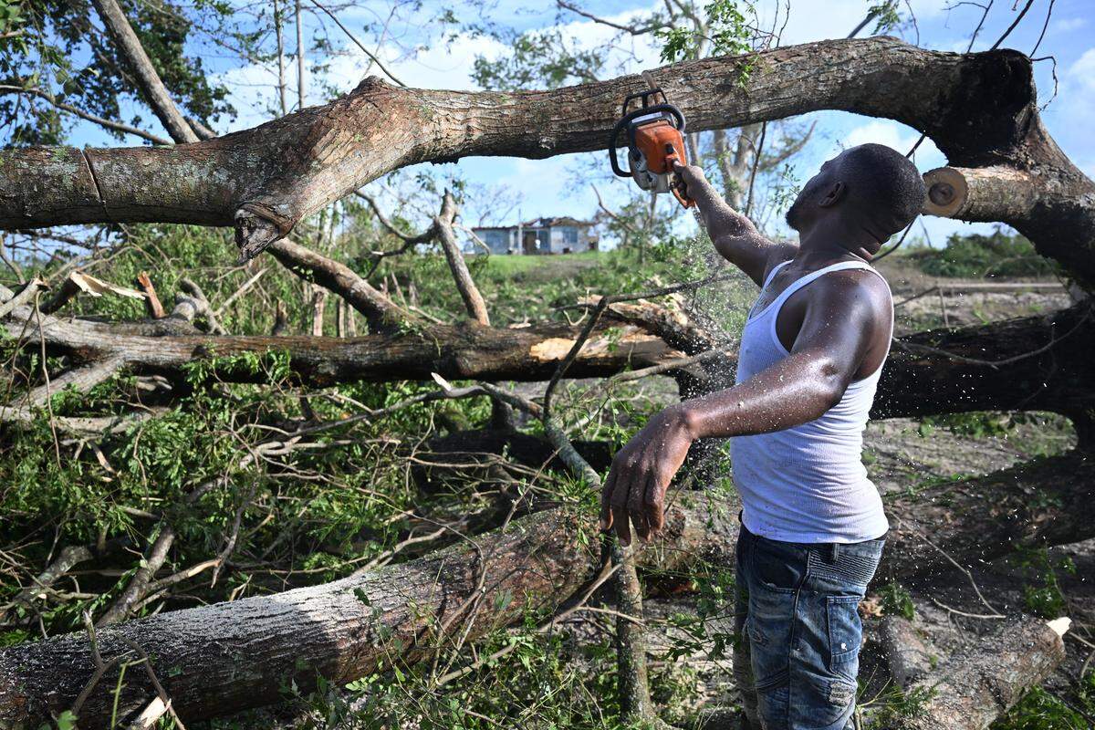 Rollin Salmond uses an electrical saw to cut sections of a tree blocking the entrance to his home in Longwood, St Elizabeth, Jamaica on October 29, 2025. Hurricane Melissa ripped up trees and knocked out power after making landfall in Jamaica on October 28, 2025 as one of the most powerful hurricanes on record, inundating the island nation with rains that threaten flash floods and landslides. 