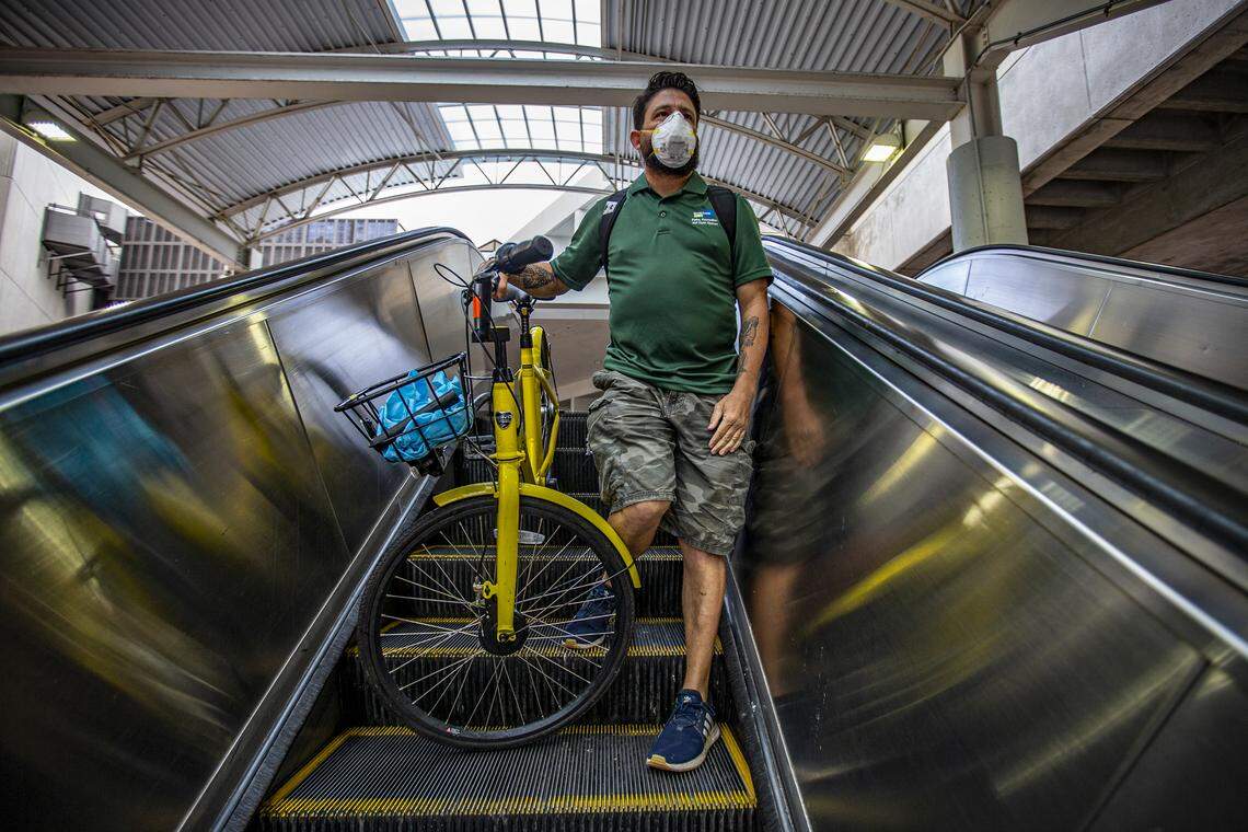 Andrew Cendan, 42, rides the escalator with his bike as he commutes to work by Metrorail while wearing a protective mask during the COVID-19 pandemic in downtown Miami on Wednesday, April 1, 2020.