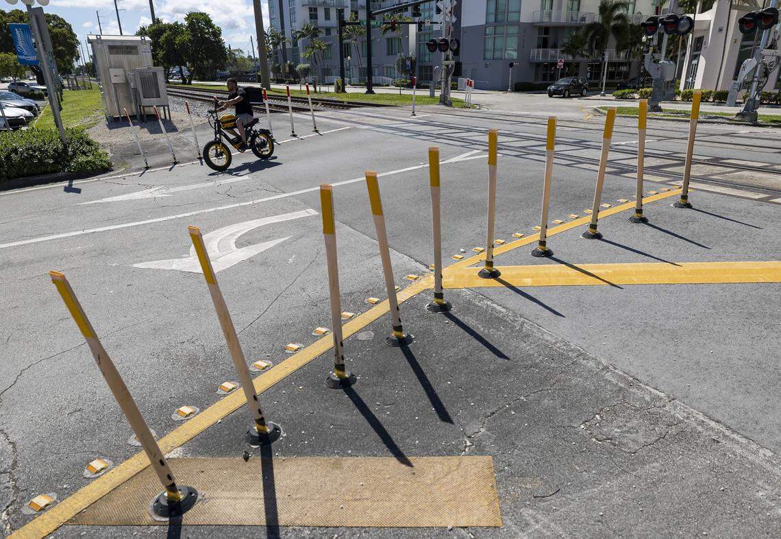White delineator posts with yellow reflective strips guide traffic near train tracks at the Harrison Street rail crossing in Hollywood, Florida.