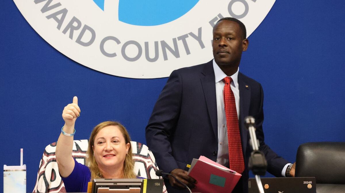 Howard Hepburn, right, walks back to his seat on the dais after being sworn into the office of superintendent of Broward County Public Schools on Wednesday, May 29, 2024, inside the boardroom of the Kathleen C. Wright Administration Center in Fort Lauderdale, Florida. On the left, Broward School Board Chair Lori Alhadeff raises a thumbs-up in the air.