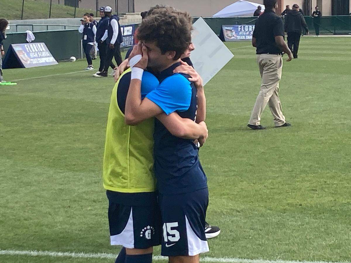 Gulliver sophomore Bruno Ripalda (right) hugs a teammate following the Raiders’ 3-2 loss to Delray American Heritage in the Class 3A state boys’ soccer semifinal on Tuesday at Spec Martin Stadium in DeLand, Fla.