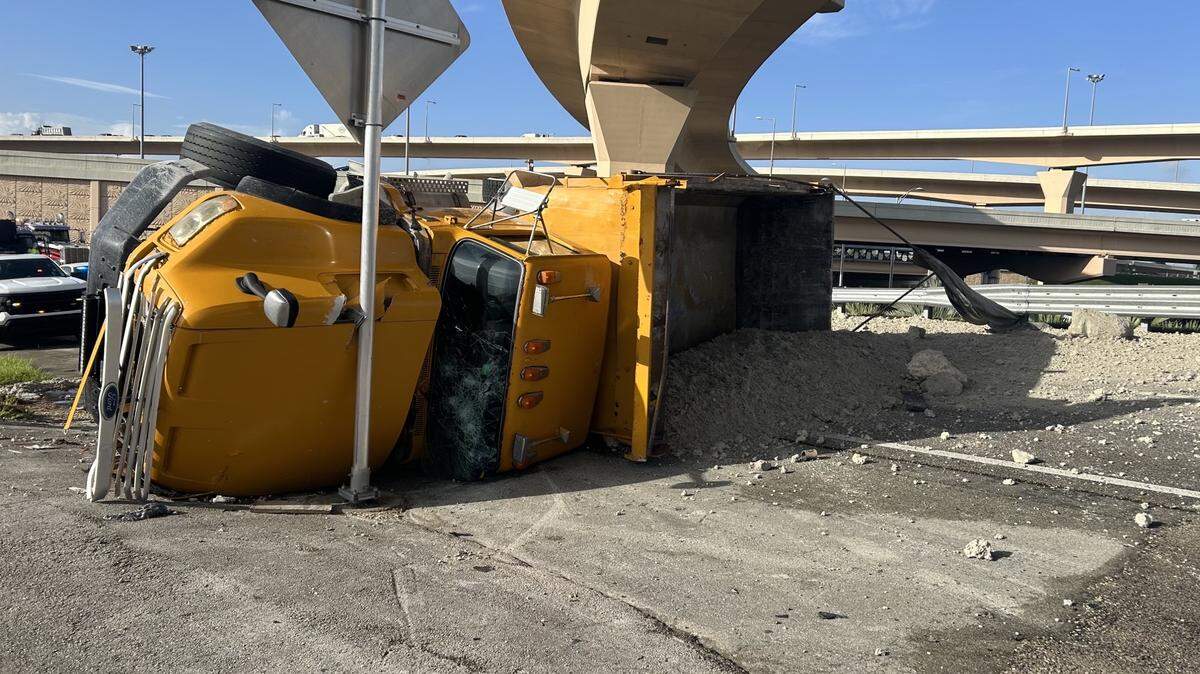 A yellow dump truck is on its side, spilling sand and gravel, after it overturned on the entrance ramp to the Palmetto Expressway Friday, Aug. 18, 2023.