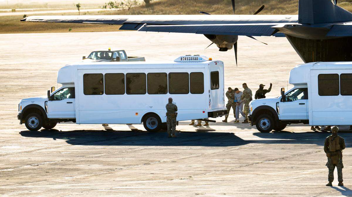 Security forces lead a man in gray sweatsuit away from a a military cargo plane that transported deportees from El Paso, Texas, to Guantánamo Bay, Cuba on Friday, Feb. 7, 2025. Doug Mills/The New York Times