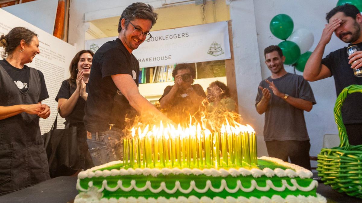 El fundador de Bookleggers, Nathaniel Sandler, apagando 101 velas mientras los invitados celebran el 12do aniversario de la librería sin fines de lucro durante un concurso de repostería en Bakehouse Art Complex el sábado 13 de julio de 2024, en Miami, Florida.