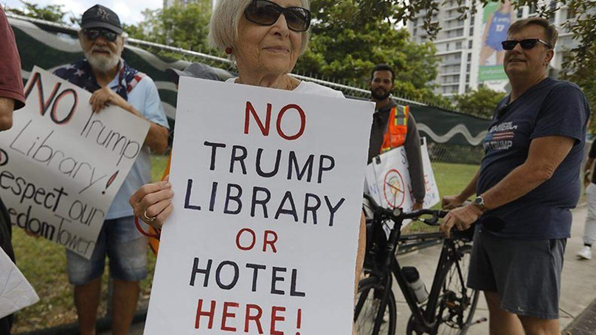Mary Alice Pilafian holds a sign reading “No Trump Library” during a demonstration outside the Kaseya Center, where former President Donald Trump appeared on Wednesday, Nov. 5, 2025, in Miami. Protesters carried signs and chanted against his policies and a proposed land transfer for Trump's presidential library, raising concerns about public accountability and local institutions.