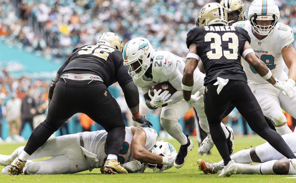 Miami Dolphins running back De'Von Achane (28) runs with the ball as New Orleans Saints defensive tackle Davon Godchaux (92) and safety Jonas Sanker (33) defend in the first half of their NFL game at Hard Rock Stadium on Sunday, Nov. 30, 2025, in Miami Gardens, Fla.