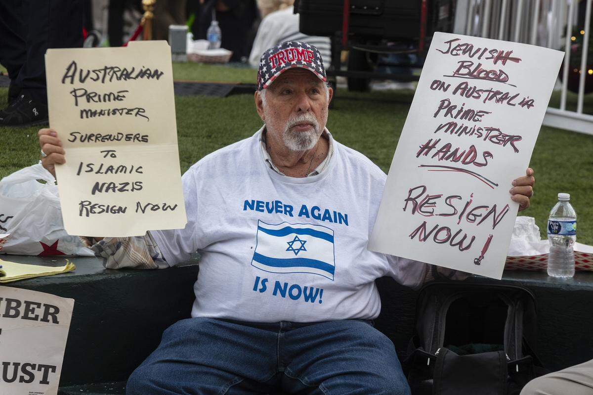 Bob Kunst holds protest signs criticizing Australia’s prime minister and condemning a shooting in Australia during a Hanukkah festival and grand menorah lighting on Lincoln Road. The death toll from the attack in Sydney has risen to 15, with 38 people still hospitalized, according to police.