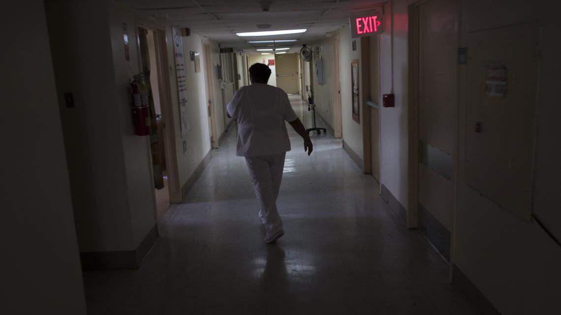 In this September 2017 file photo, a nurse walks through a darkened wing at a hospital in Puerto Rico. A nurse recruited to work in the U.S. says MedPro Healthcare Staffing, the South Florida company that paid for her travel and helped her get a green card, threatened to report her for immigration fraud and sued for $150,000 after she broke her contract.