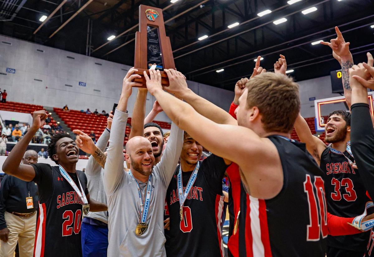 Sagemont High School basketball coach Andrew Moran holds the State Championship Trophy as he celebrates with players after defeating Orlando Christian Prep during the FHSAA Class 2A Final at the RP Funding Center in Lakeland, Florida on Friday, March 3, 2023.