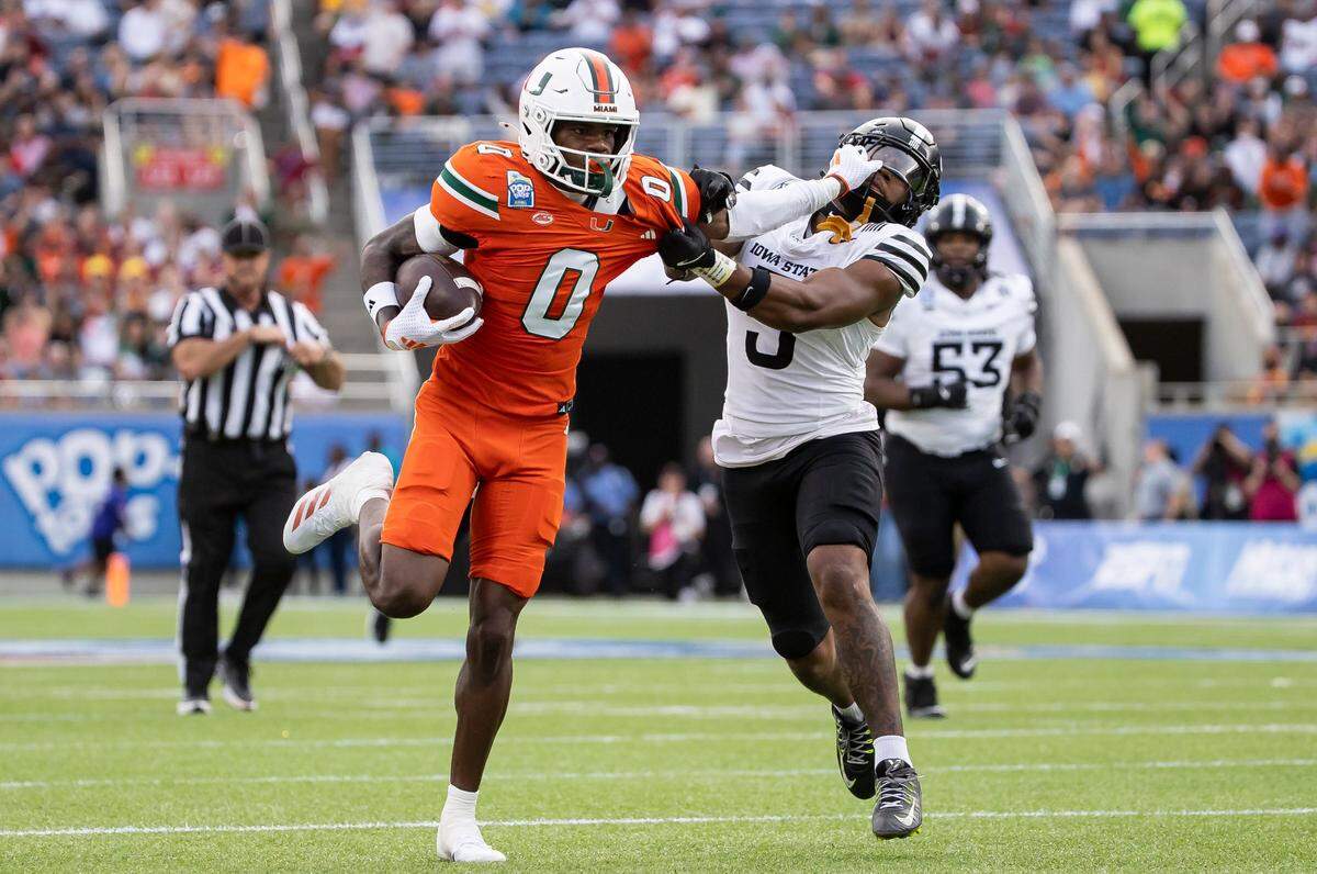 Miami Hurricanes wide receiver Joshisa Trader (0) stiff-arms Iowa State Cyclones defensive back Myles Purchase (5) as he runs with the ball to score a touchdown in the first half of their Pop-Tarts Bowl football game at the Camping World Stadium on Saturday, Dec. 28, 2024, in Orlando, Fla.