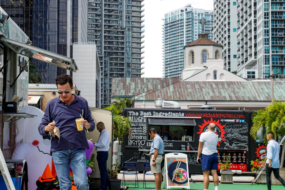 A man holding a drink walks away while others wait in line to place an order from a food truck at the First Miami Presbyterian waterfront parking lot at 609 Brickell Ave. in Miami, Florida, on Tuesday, Oct. 12, 2021.