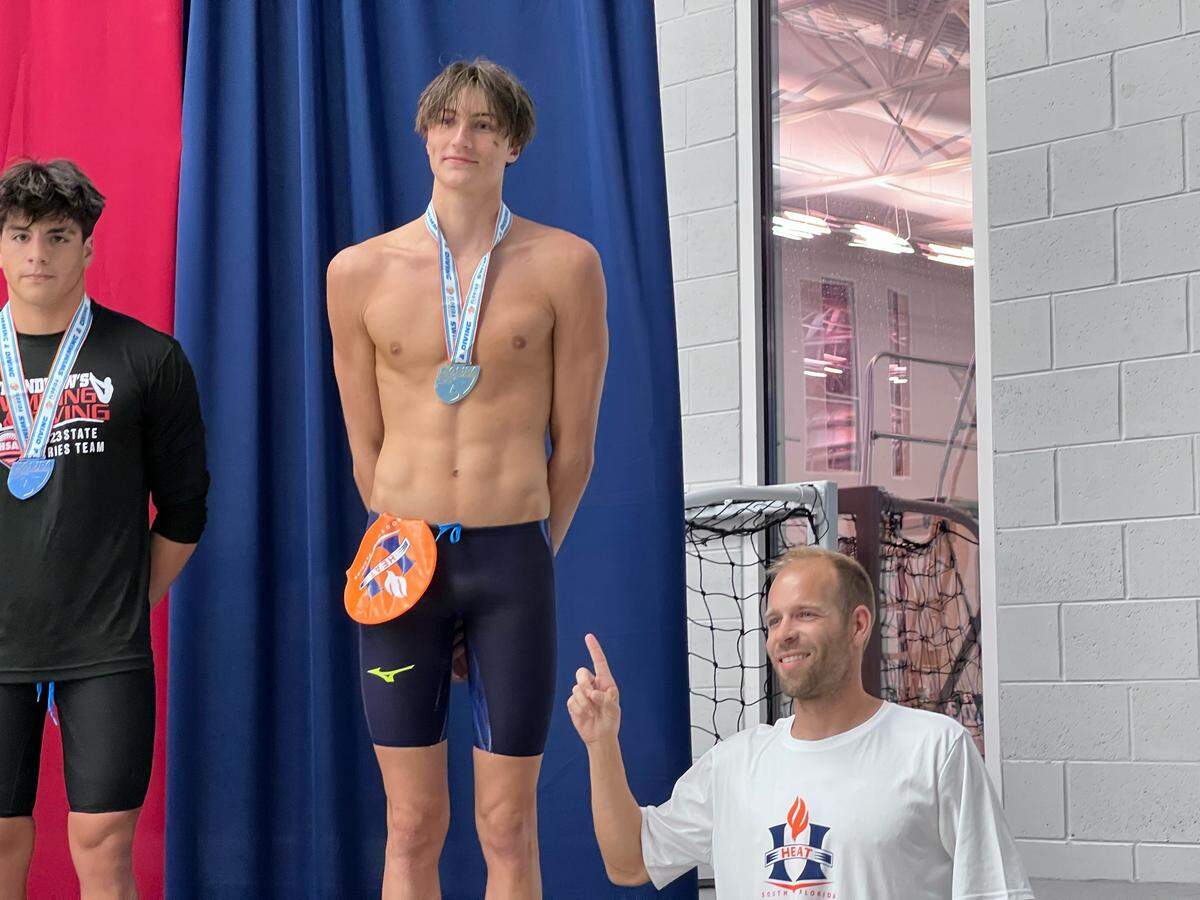 South Florida HEAT boys’ swimmer Kaii Winkler (left) celebrates at the podium with his coach Adam Madarassy (right) after breaking one of two national records at Saturday’s Class 1A state championships in Ocala.