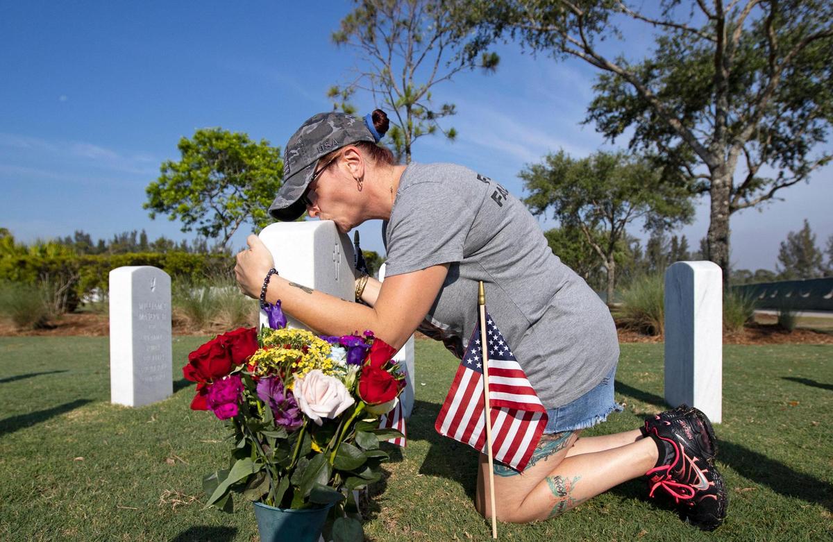 Anne Marie Oto kisses the tombstone of her father, Korean War veteran Godfrey Thomas, at the South Florida National Cemetery in Lake Worth on Sunday. She was a volunteer who placed American flags on some 25,000 graves in preparation for a Memorial Day ceremony.