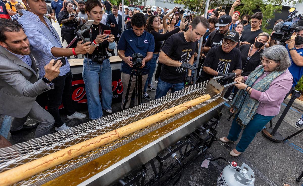 Miami, Florida, October 1, 2021 - Miami-Dade County Mayor, Daniella Levine Cava along with the help of a Sergio’s employee, right, lift the croqueta slightly off the hot cooking oil as Carlos Gazitua, President and CEO of Sergio’s Restaurant, directs their movements as they attempt to make the world’s longest croqueta.