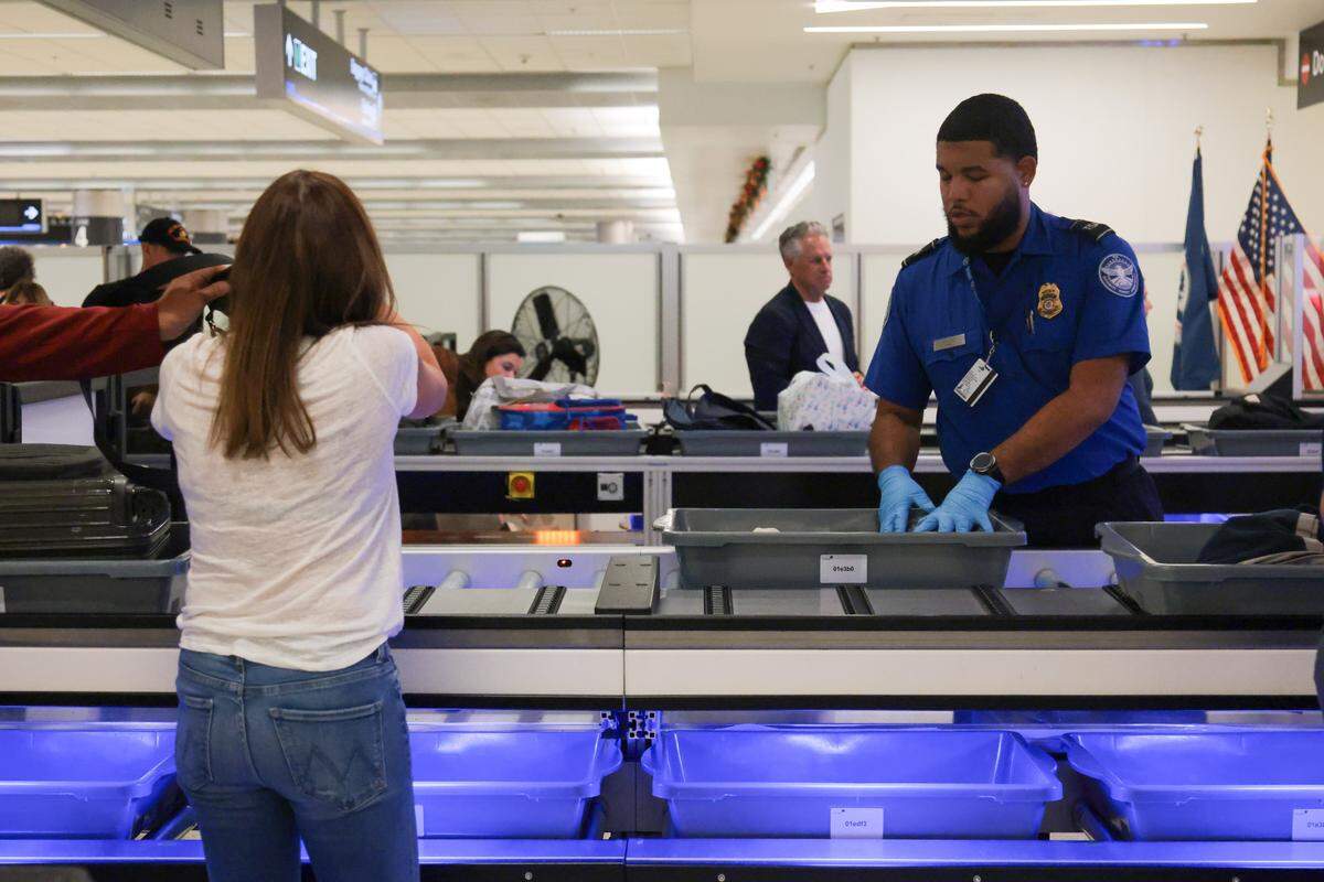 A TSA agent directs a traveler to place her luggage and belongings inside a bin on a lane with an automated bin return system during a standard security screening at checkpoint 2 at Miami International Airport on Tuesday, Nov. 25, in Miami, Fla.