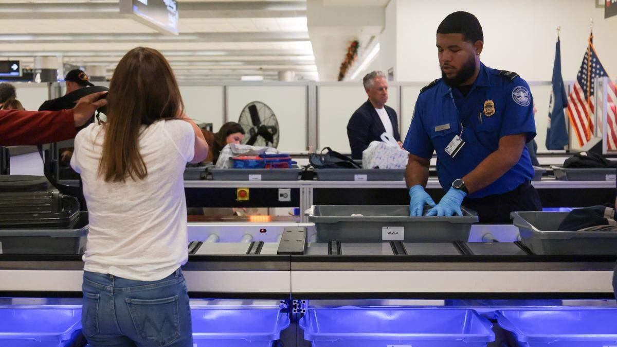 A TSA agent directs a traveler to place her luggage and belongings inside a bin on a lane with an automated bin return system during a standard security screening at checkpoint 2 at Miami International Airport on Tuesday, Nov. 25, in Miami, Fla.