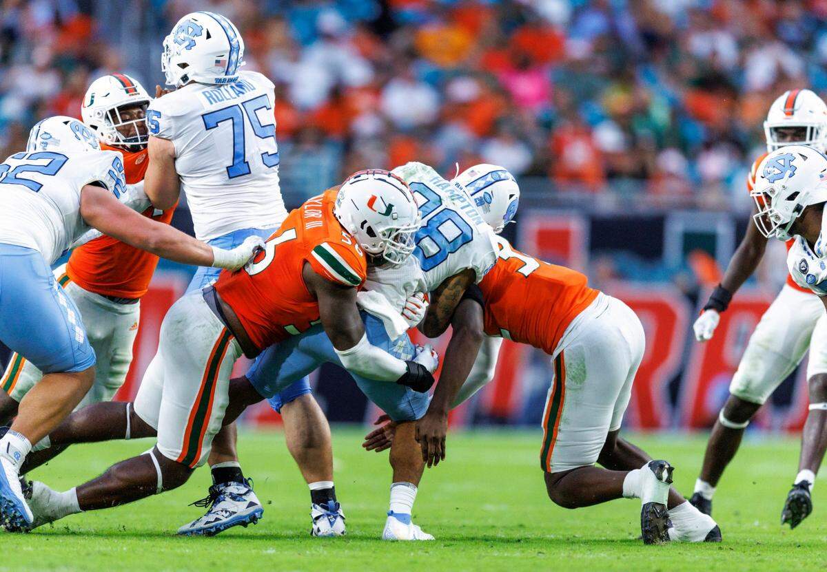 Miami Hurricanes defensive linemans Leonard Taylor III (56) and Nyjalik Kelly (32) bring down North Carolina Tar Heels running back Omarion Hampton (28) during the fourth quarter of an ACC conference football game at Hard Rock Stadium on Saturday, October 8, 2022 in Miami Gardens, Florida..