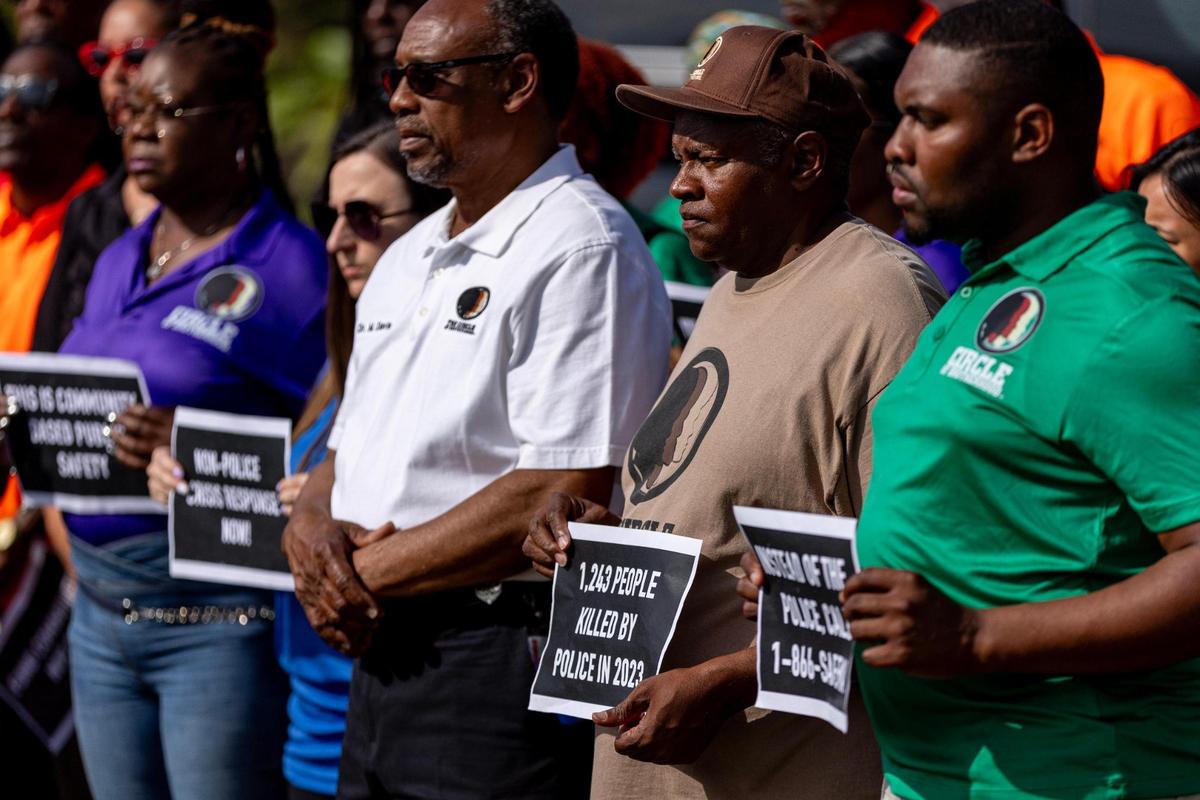 Members of The Circle of Brotherhood, Dream Defenders, Peacemakers, Touching Miami with Love and Dade County Street Response hold signs that read ‘People With Mental Illness Are More Likely To Be Killed By Police’, “1,243 People Killed By Police In 2023’ and “Fund Communities Not Cops” during a press conference held by the Healing and Justice Center across the street from the scene of a shooting at NW 58th St and NW 7th Court, in Liberty City, Florida, on Thursday, March 14, 2024. City of Miami police officers shot Donald Armstrong last week more than five times while responding to an emergency call during a mental health crisis.