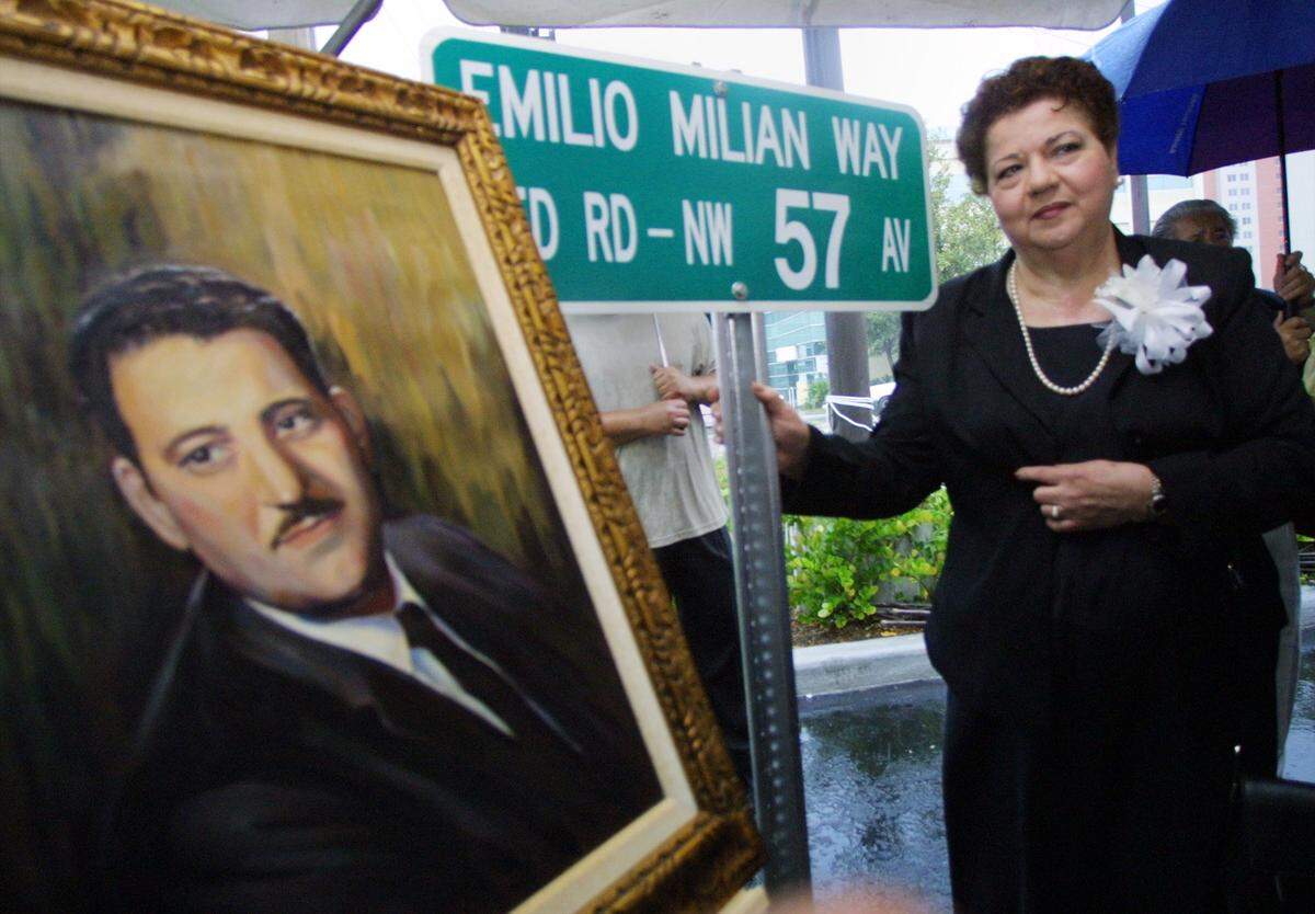Mirta Milian stands next to a painiting and street sign in memory of her late husband Emilio Milian Sr. on Aug 1, 2001.