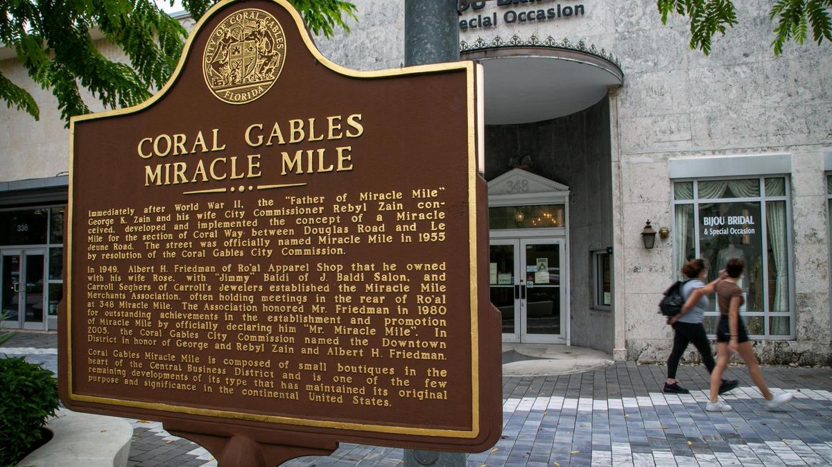 Pedestrians walk by a marker explaining the origins of Miracle Mile.