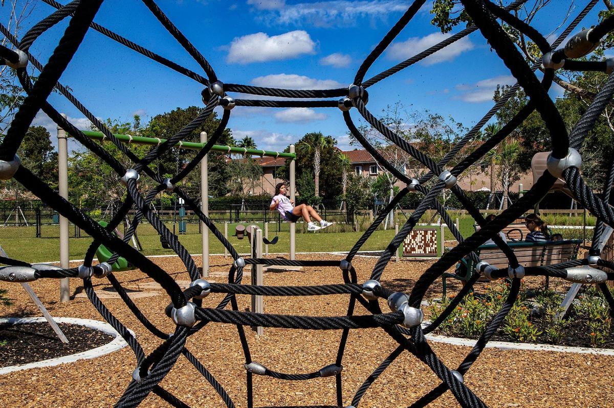 Kids swing in the playground at west Miami-Dade’s new Tree Island Park, as seen through a climbing net. The 113-acre county park in the middle of dense suburban sprawl contains a 70-acre piece of restored Everglades prairie and tree islands, or hardwood hammocks.