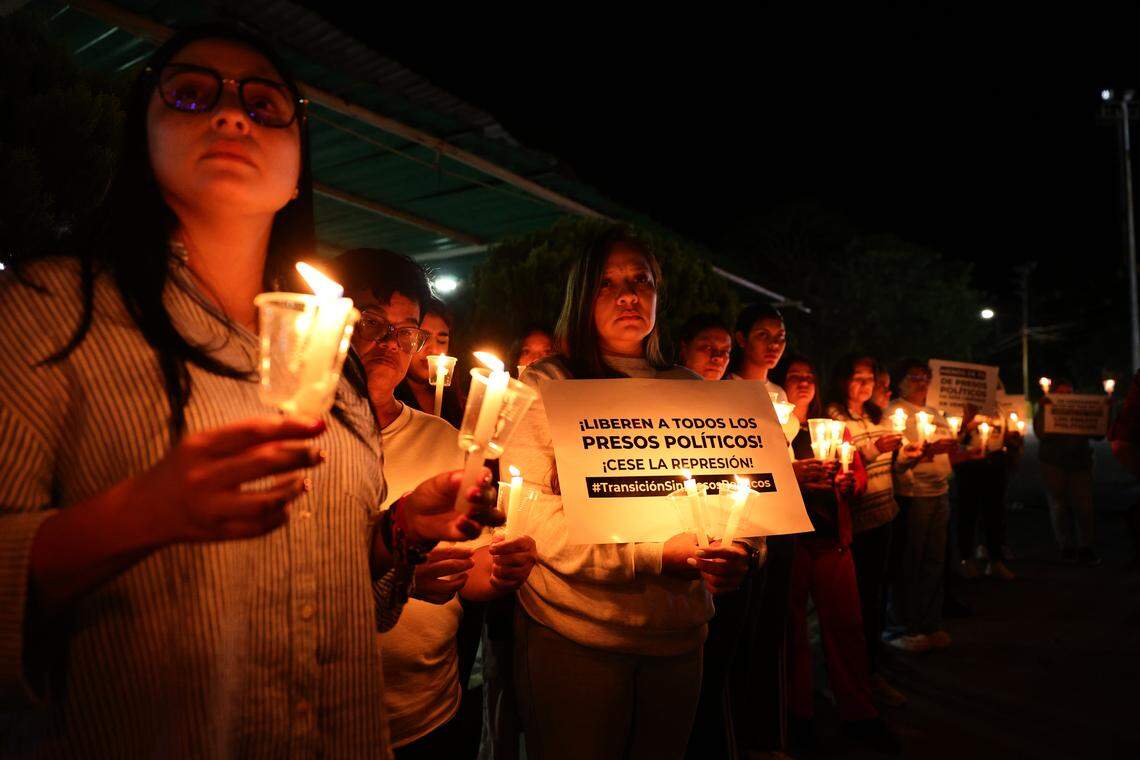 A relative of prisoners holds candles and a sign that reads in Spanish "¡Liberen a todos los presos politicos! ¡Cese la represión!" (Free all political prisoners. Stop the repression) during a vigil while waiting updates on the release of prisoners outside El Rodeo prison on Friday, Jan. 09, 2026, in Miranda, Venezuela. 