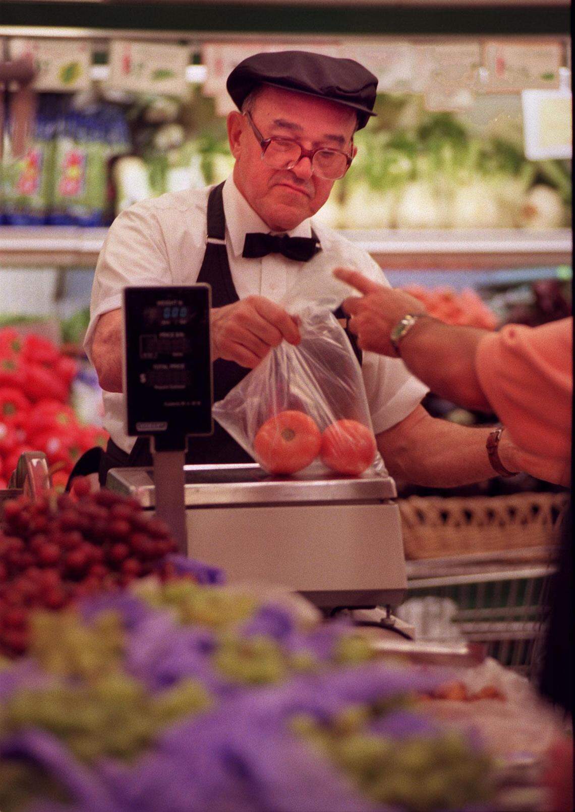 Epicure employee Alberto Serpa weighs tomatoes for a customer.