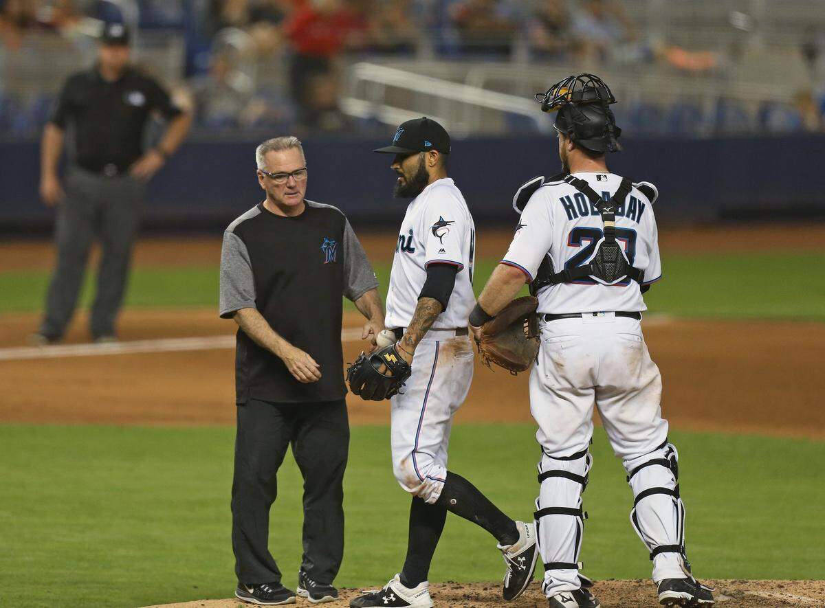 Miami Marlins catcher Bryan Holaday (28) looks as Marlins assistant certified athletic trainer Mike Kozak treating Miami Marlins pitcher Sergio Romo (54) after he collide with Washington Nationals second baseman Brian Dozier (9) during the ninth inning of an Major League Baseball game at Marlins Park in Miami on Thursday, June 27, 2019.