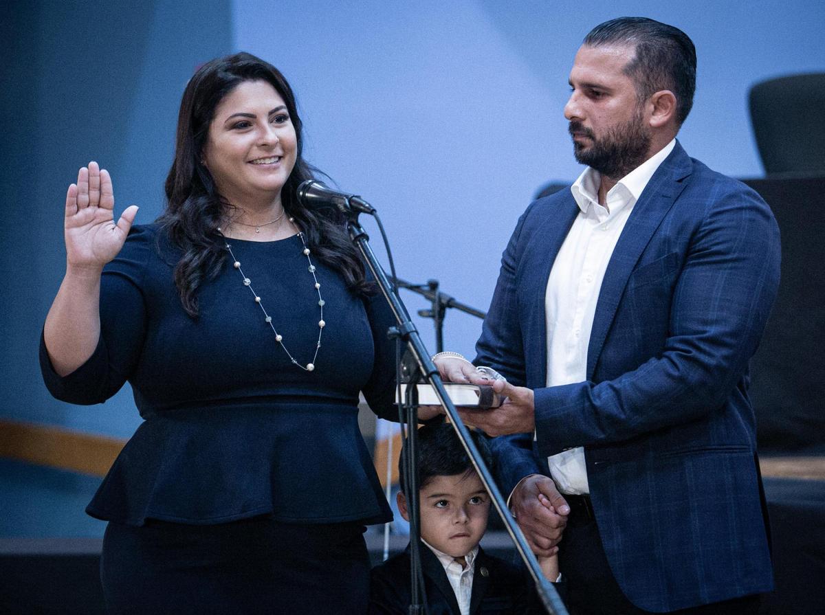 Christi Fraga, 33, an ice cream shop owner, raises her hand as she is sworn in to the Miami-Dade School Board on Tuesday. Her husband, Gabriel, holds the Bible. Standing by under the mic is their son Gabriel Jr.